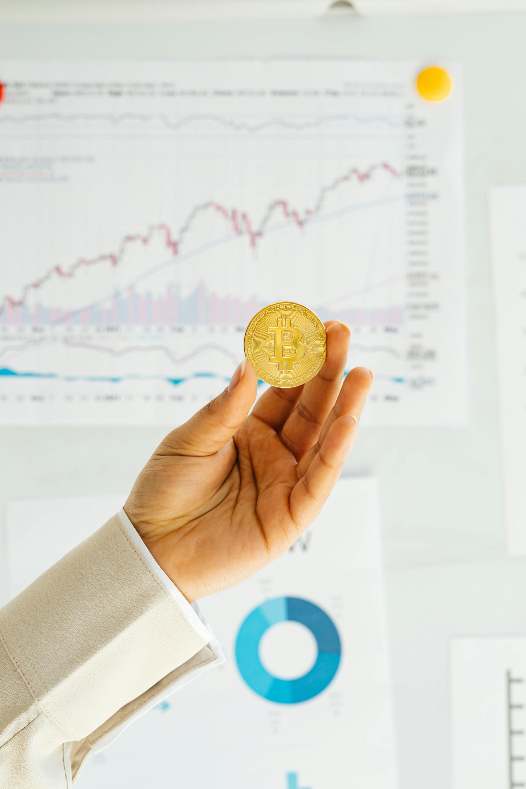 A woman holding a bitcoin with financial charts in an office setting.